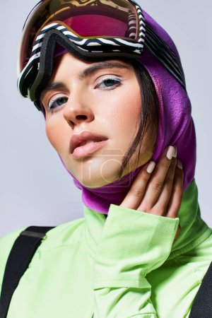 portrait of woman in ski clothes with balaclava looking at camera on grey, model with blue eyes