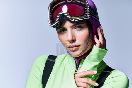 Téléchargez les photos : Portrait de femme en tenue active avec cagoule violette sur la tête regardant la caméra sur fond gris - en image libre de droit