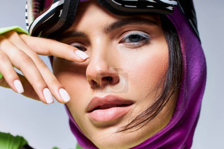 close up of woman in active wear with purple balaclava on head looking at camera on grey background