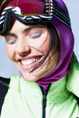 Foto de Primer plano de mujer alegre en desgaste activo con pasamontañas en la cabeza sonriendo sobre fondo gris - Imagen libre de derechos