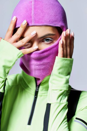 Photo for Portrait of woman with blue eyes wearing purple ski mask and looking at camera on grey backdrop - Royalty Free Image