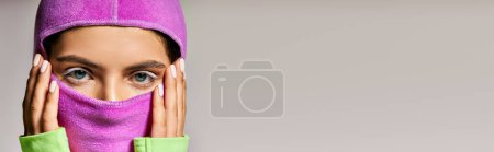 Photo for Close up of woman with blue eyes wearing ski mask and looking at camera on grey backdrop, banner - Royalty Free Image