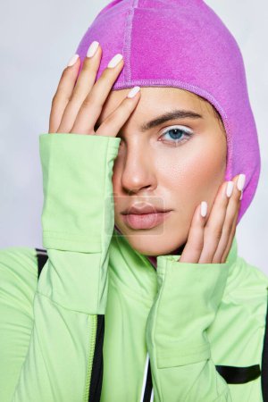 portrait of beautiful woman with blue eyes posing in warm ski mask and active wear on grey backdrop