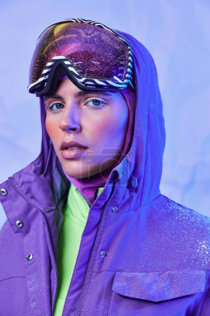 hermosa mujer en máscara de esquí y googles usando chaqueta caliente sobre fondo púrpura, estilo invierno