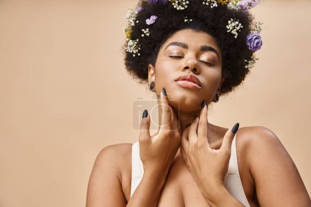 sensual african american woman with colorful flowers in hair posing with closed eyes on beige