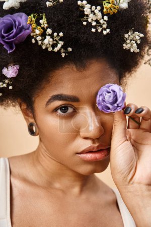 close up portrait of african american woman with floral decor in hair and flower near face on beige