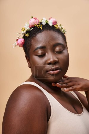 portrait of african american plus size woman with colorful flowers in hair and closed eyes on beige