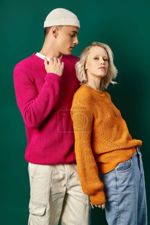 stylish young couple in winter sweaters posing and looking at camera on turquoise background