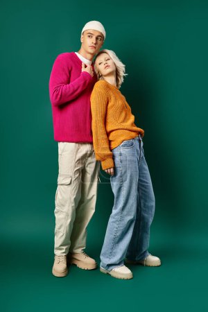 full length of stylish young couple in winter sweaters posing together on turquoise background
