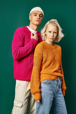 stylish young models in winter sweaters posing and looking at camera on turquoise background