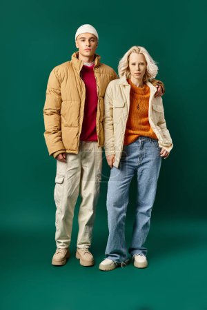 stylish couple in winter puffer jackets posing together on turquoise background, young man and woman