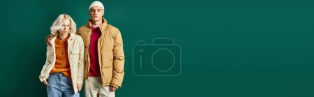 stylish man in winter puffer jacket hugging woman and posing together on turquoise backdrop, banner