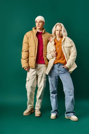 couple in winter puffer jackets posing together on turquoise background, stylish man and woman