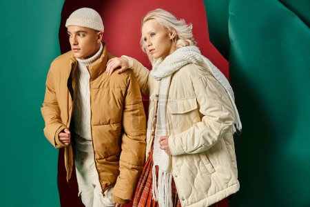 stylish man in beanie and puffer jacket posing with blonde woman on red with turquoise backdrop