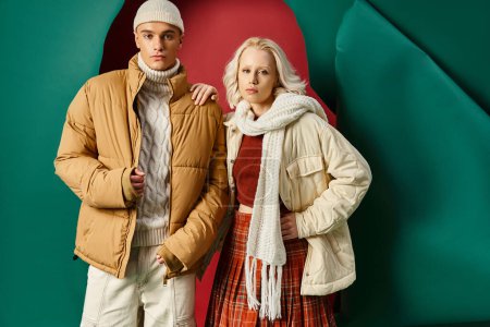 young man in beanie and puffer jacket posing with blonde woman on red with turquoise backdrop