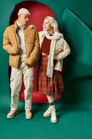 young blonde woman in plaid skirt posing with man in winter attire on red with turquoise backdrop