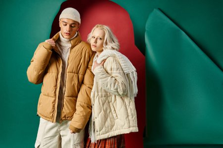 stylish young couple in white winter jackets posing together on red with turquoise backdrop