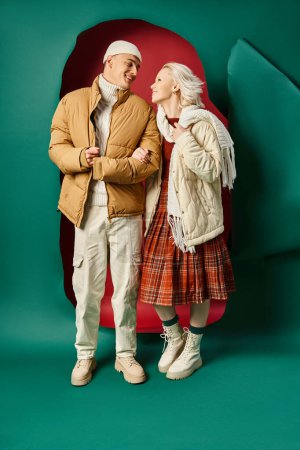 Foto de Larga duración de feliz pareja en chaquetas de invierno blancas posando juntos en rojo con fondo turquesa - Imagen libre de derechos