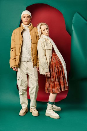 Foto de Longitud completa de la pareja en chaquetas de invierno de moda posando juntos en rojo con fondo turquesa - Imagen libre de derechos