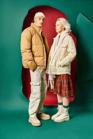 Foto de Longitud completa de la pareja en chaquetas de invierno modernas posando juntos en rojo con fondo turquesa - Imagen libre de derechos