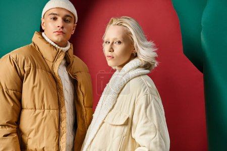 Foto de Retrato de pareja en chaquetas de invierno posando con las manos en bolsillos en rojo con fondo turquesa - Imagen libre de derechos