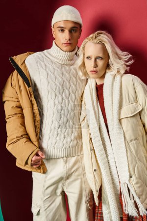 fashionable man and woman in winter outerwear posing together on torn turquoise and red background