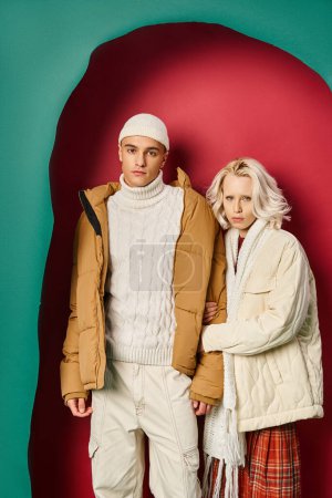 femme blonde en vêtements d'hiver blanc tenant la main de l'homme près de turquoise déchiré et fond rouge