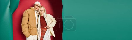 attractive woman and man in winter outerwear posing near torn turquoise and red backdrop, banner