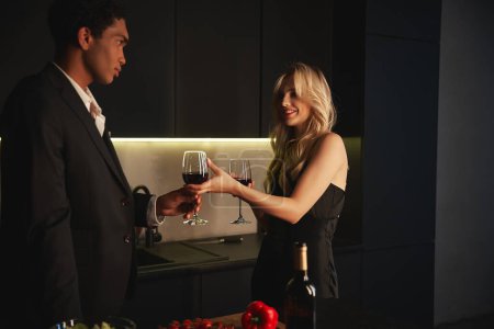 handsome african american man in elegant suit taking glass of red wine from his jolly girlfriend