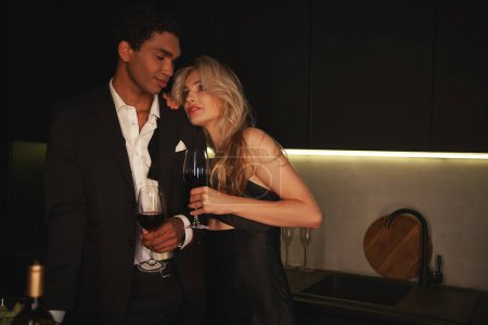 Liebendes junges multiethnisches Paar, das abends zusammen Zeit mit Rotwein im Glas verbringt