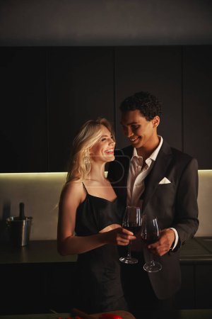 Téléchargez les photos : Joyeux jeune couple multiculturel en tenues élégantes profiter l'un de l'autre et tenant des verres à vin - en image libre de droit