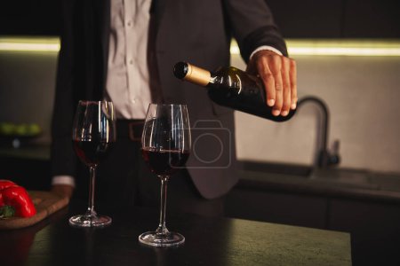 Photo for Cropped view of young african american man in elegant chic suit pouring red vine into glasses - Royalty Free Image