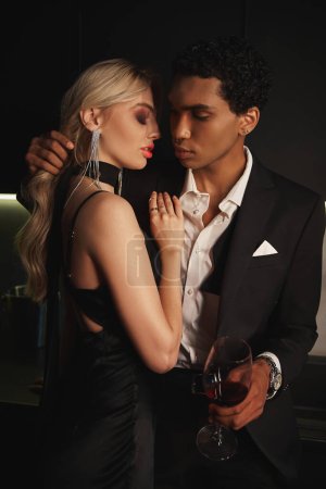 Téléchargez les photos : Attrayant couple multiracial aimant se préparant à embrasser allègrement, verre de vin rouge à la main - en image libre de droit