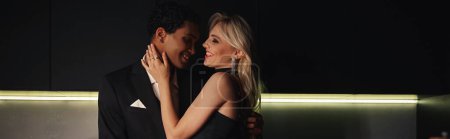 Téléchargez les photos : Couple multiculturel gai en tenue chic étreignant chaleureusement et souriant à l'autre, bannière - en image libre de droit