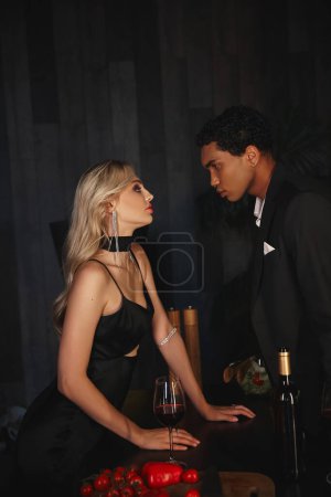 buen aspecto joven pareja interracial en elegantes atuendos mirando sensualmente el uno al otro en la cocina
