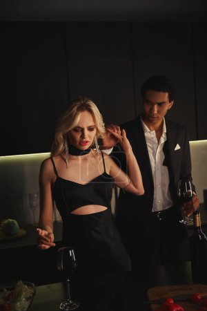mujer hermosa enojada en vestido negro posando junto a su novio afroamericano con copa de vino