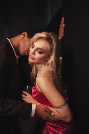 Foto de Pareja interracial sensual de buen aspecto con accesorios que se preparan para besar amorosamente mientras están en casa - Imagen libre de derechos