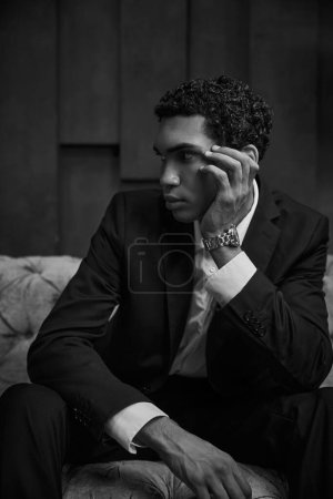 Schwarz-Weiß-Foto eines attraktiven jungen afrikanisch-amerikanischen Mannes im schicken Anzug, der sitzt und wegschaut