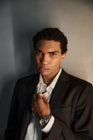 attraktiver junger afrikanisch-amerikanischer Mann im schwarzen eleganten Anzug blickt vor grauem Hintergrund in die Kamera