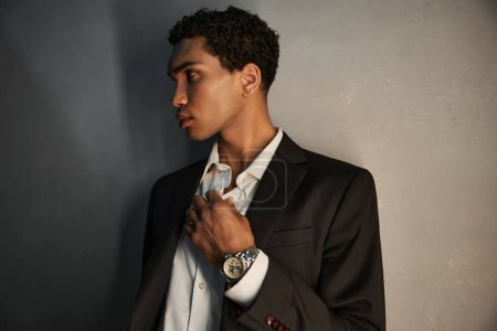 good looking young african american man with accessories in black suit posing and looking away