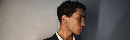 atractivo joven afroamericano hombre con accesorios en traje negro posando y mirando hacia otro lado, pancarta