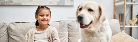 fille heureuse assise sur le canapé avec labrador mignon dans le salon moderne, compagnon animal, bannière