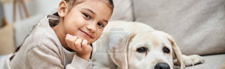 portrait of happy girl smiling near cute labrador in modern living room, pet with  child banner
