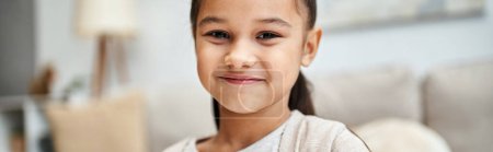 Téléchargez les photos : Portrait de heureuse fille d'âge élémentaire avec des cheveux bruns souriant dans un appartement moderne, bannière - en image libre de droit