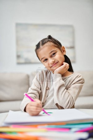 Porträt eines süßen Mädchens im Grundalter, das mit Farbstift auf Papier in einer modernen Wohnung zeichnet
