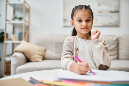 little cute elementary age girl drawing with color pencil on paper in modern apartment