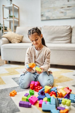 niedliches kleines Mädchen spielt mit bunten Spielzeugklötzen auf Teppich im Wohnzimmer, Turmbau-Spiel