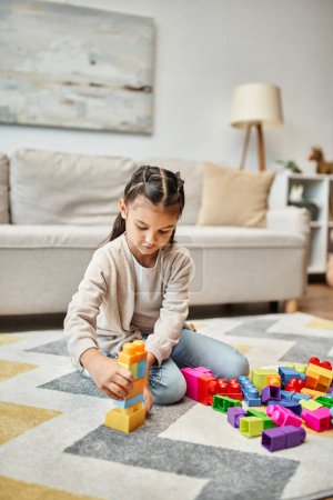 elementary age girl playing with colorful toy blocks on carpet in living room, building tower game