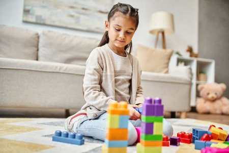 Foto de Linda chica jugando con bloques de juguete de colores en la alfombra en la sala de estar, la construcción de la torre juego - Imagen libre de derechos
