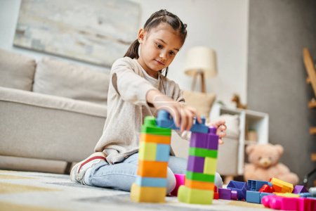linda chica jugando con bloques de juguete de colores en la alfombra en la sala de estar moderna, la construcción de la torre juego